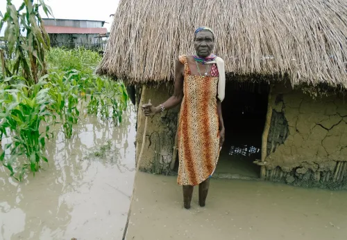 Criteria: Bejaarde dame in Zuid-Soedan staat voor haar huis, dat tot aan de ingang onder water staat